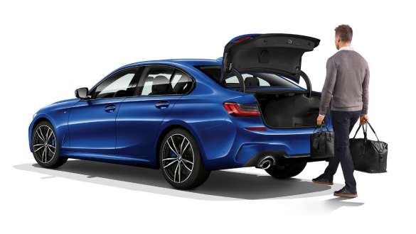 Three-quarter rear shot of standing BMW 3 Series Sedan with driver automatically opening the tailgate with his foot.